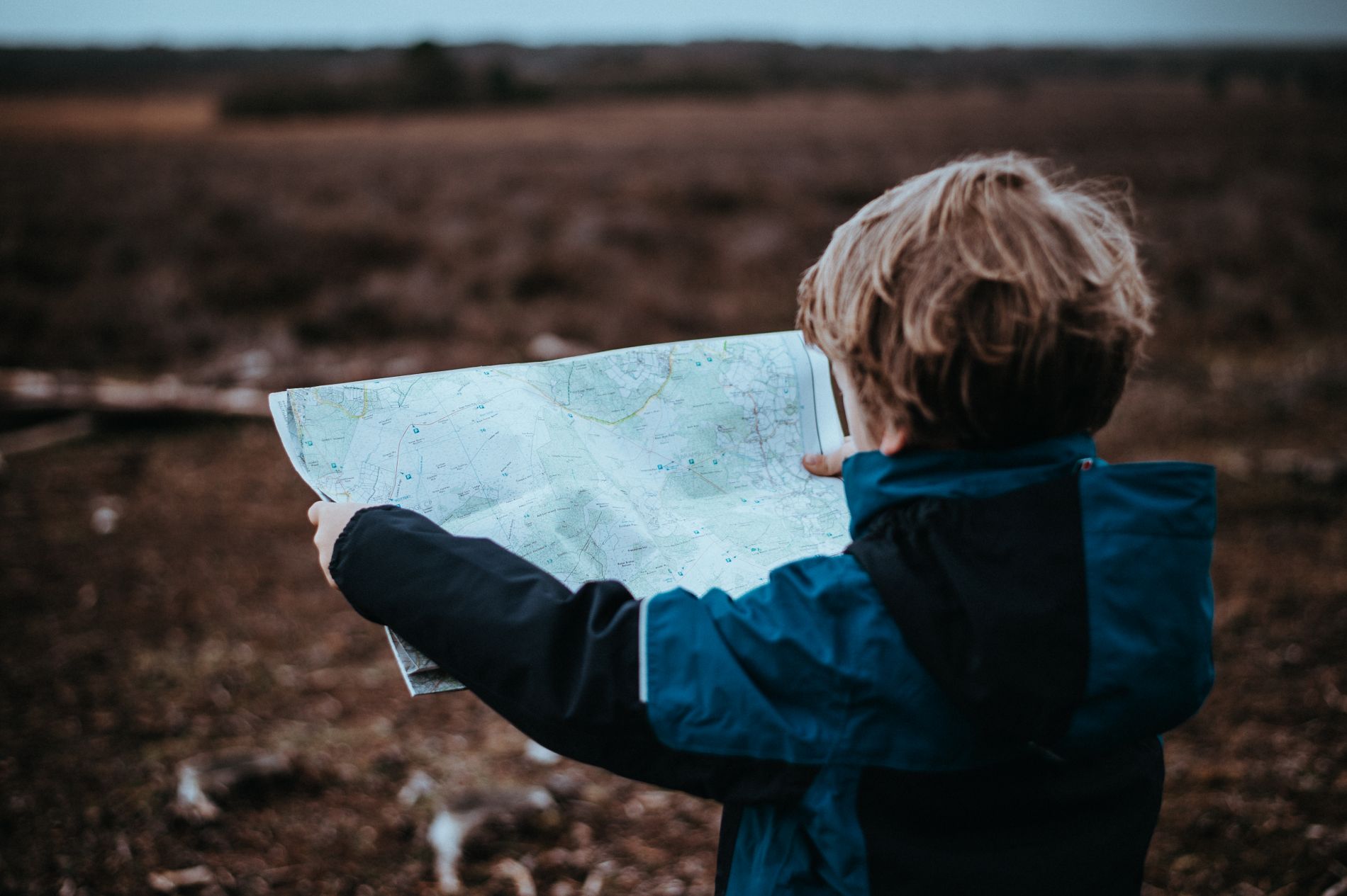A young boy, facing away from the camera, holds a folded paper map with both hands