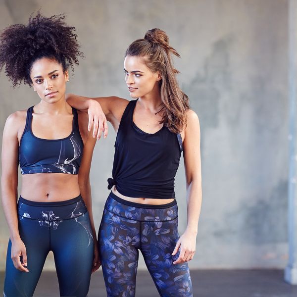 Two young women stand side by side posing in athletic attire