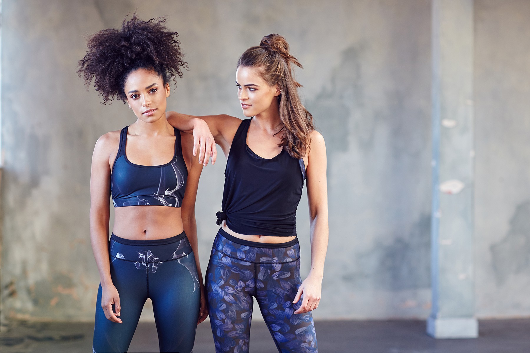 Two young women stand side by side posing in athletic attire