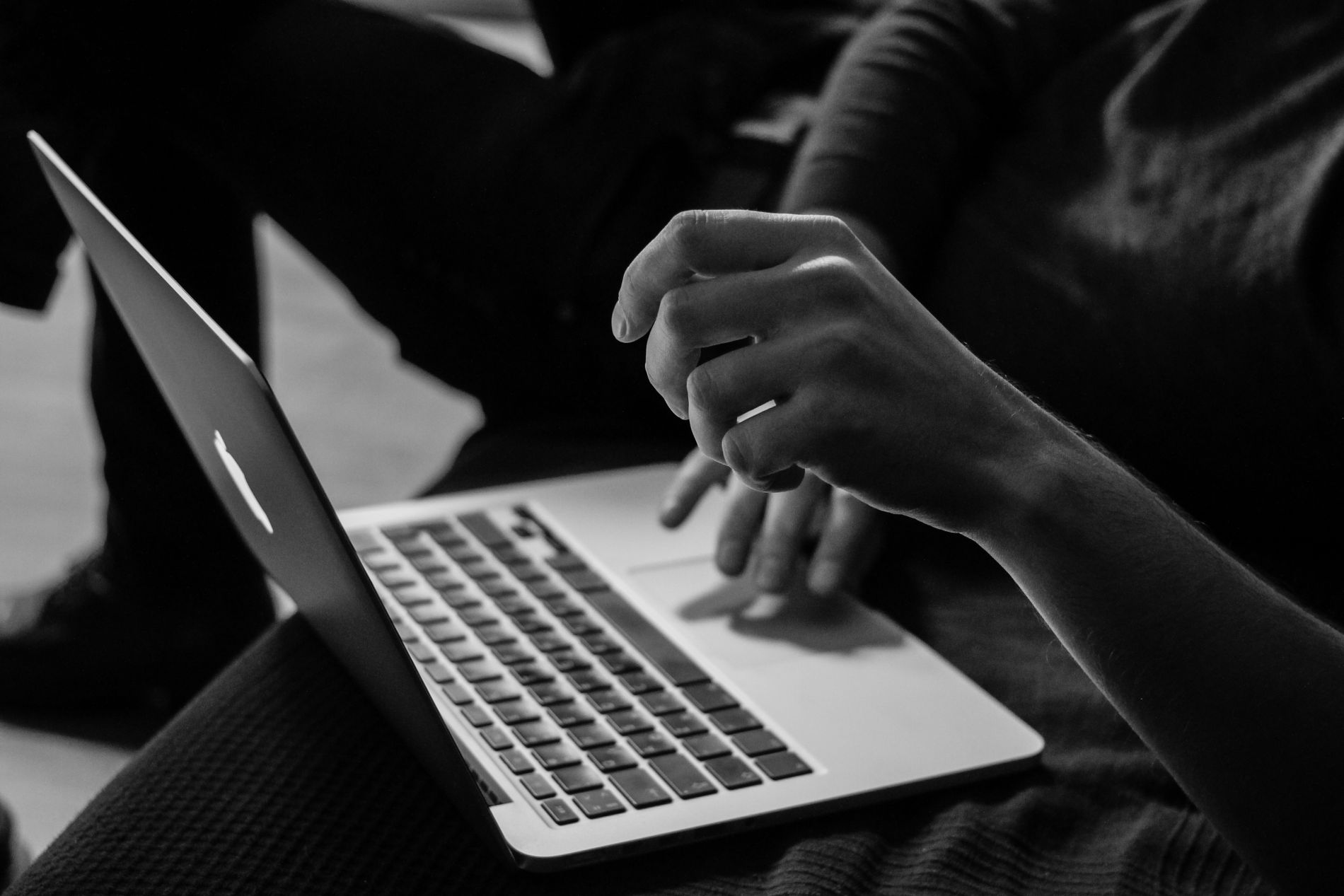 A person uses their Apple Macbook laptop while seated