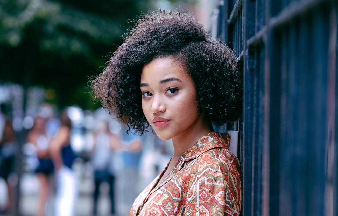 Actress Amandla Stenberg leans against a fence in an urban setting