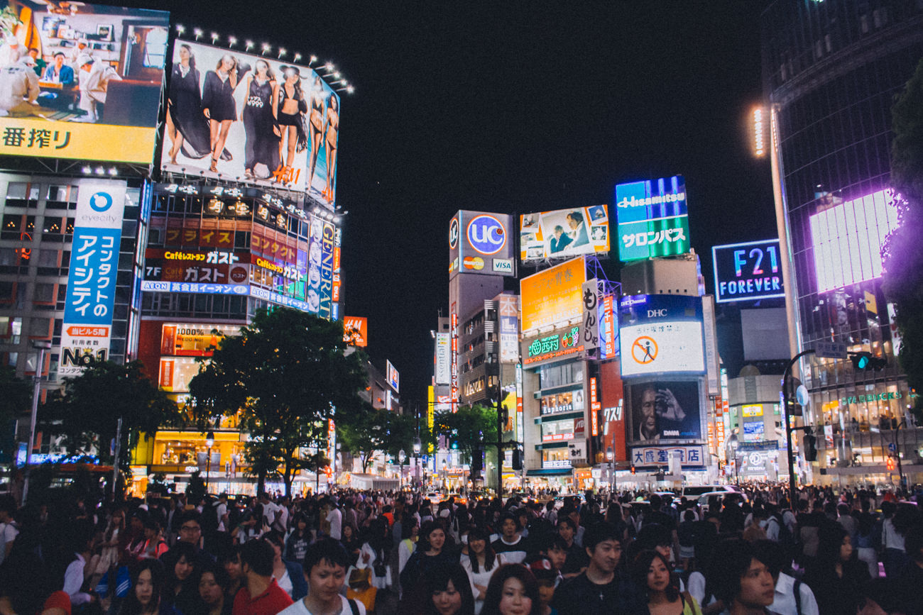 A crowd of people move through Shibuya Crossing in Tokyo, Japan at night, surrounded by billboards