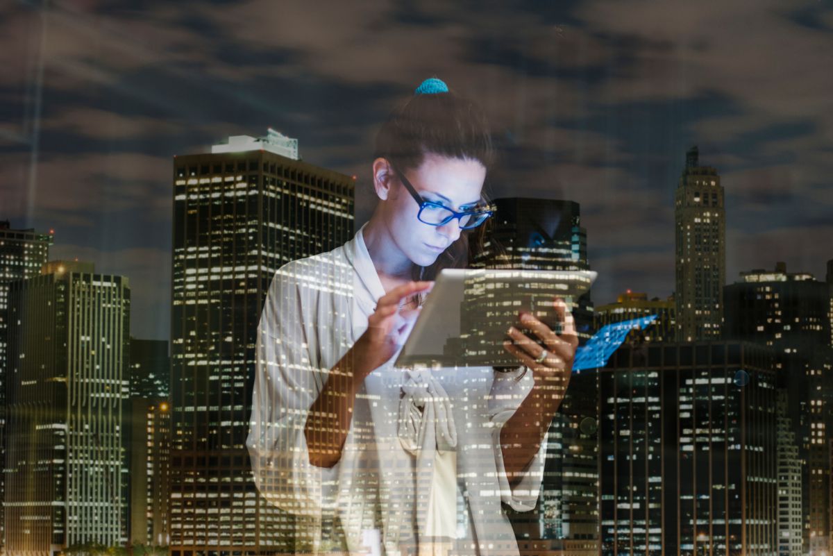 Young woman using digital tablet at home against city lights