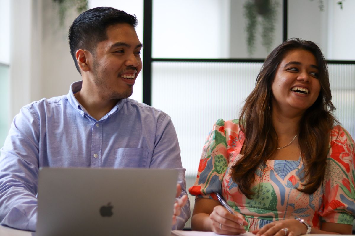 Image shows two JBi employees sat side by side laughing